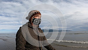 Man walking on beach in winter wearing face mask due to coronavirus