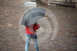 Man walking with black umbrella and red coat on cobbles place