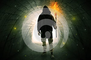 Man walking with burning flambeau in a dark tunnel