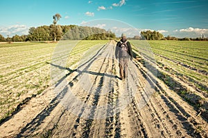 A man walking down a dirt road among fields, horizon and blue sky