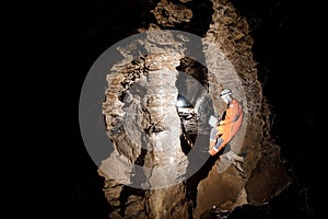 Man walking and exploring dark cave with light headlamp and map in his hand underground.