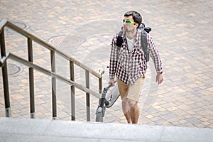 Man walking with folded electric scooter up stairs in city near modern building. Ecological technological lifestyle. E-Mobility.