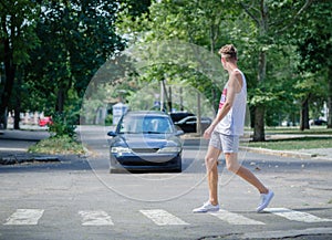 Man walking in front of a car. A boy crossing street on a blurred background. Careful on the road concept. Copy space.