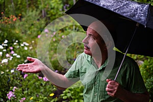 Man walking in garden with umbrella during rain.