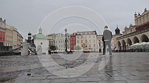 Man Walking Through Krakow Main Square, Rear view of a man walking alone across the wet cobblestone of Krakow's