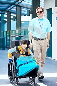 Man walking next to little boy in wheelchair outside medical facility