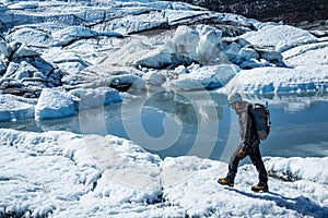 Man walking over white ice next to calm lake on the Matanuska Glacier in Alaska