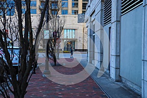 A man walking on a red brick sidewalk surrounded by colorful buildings and bare winter trees at Atlantic Station photo
