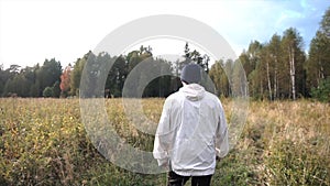 Man walking on rural road passing through green field surrounded by forest to his car, parked on horizon against sunny