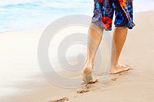 Man walking on sand beach leaving footprints in the sand. Ð¡lose up of man leg on the beach.