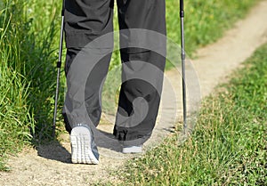 Man walking on sandy path wearing sneakers, using tracking sticks.