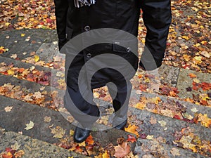 A man walking on stairs covered with autumn leaves.