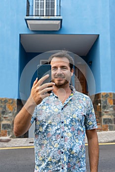 Man walking in the street with his smart phone, making a plan with his college and smiling. Caucasian hipster with beard out of