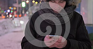 Man walking on street in warm clothing and text messaging on mobile phone at night