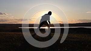 Man walking on summer meadow, sunset. Silhouette of the young man on the mountain top.