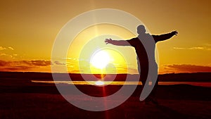 Man walking on summer meadow, sunset. Silhouette of the young man on the mountain top.