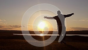 Man walking on summer meadow, sunset. Silhouette of the young man on the mountain top.