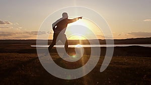 Man walking on summer meadow, sunset. Silhouette of the young man on the mountain top.