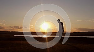 Man walking on summer meadow, sunset. Silhouette of the young man on the mountain top.