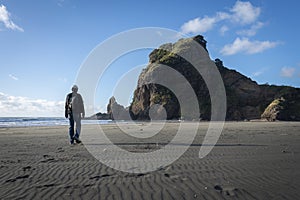 Man walking towards the Lion Rock at Piha Beach, blue sunny day. Waitakere, Auckland