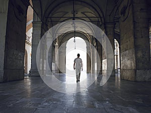 Man walking under heavy vaults, in Pisa, Italy. Bright light seeping in.