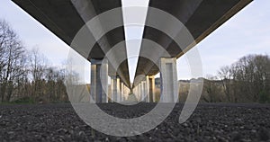 Man walking underneath highway bridge underpass structure with concrete columns.