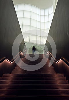 Man walking up stairs into the light in a modern and futuristic architecture