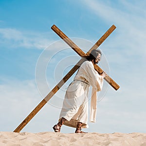 Man walking with wooden cross against blue sky in desert