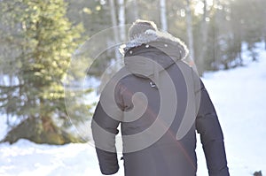 Man walking in the woods on a snowy path wearing a warm winter coat. Remote country road is idyllic for hiking.Man walking in the