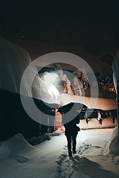 Man walkng on a snowy alley with an umbrella, at night