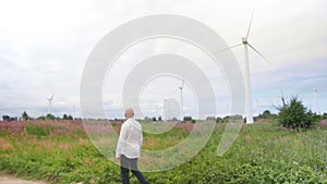 Man walks across the field against the background of wind turbines energy production. Full shot.