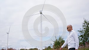 Man walks across the field against the background of wind turbines Energy Production. Medium shot.