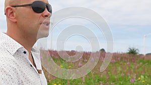 Man walks across the field and sing against the background of wind turbines Energy Production. Close up shot.