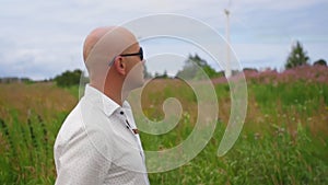 Man walks across the field and sing against the background of wind turbines Energy Production. Medium shot.