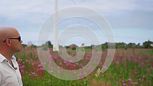 Man walks across the field and sing against the background of wind turbines energy production. Medium shot.