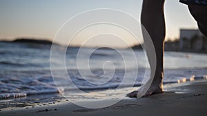 Man walks along the coastline at sunset legs close-up slow motion