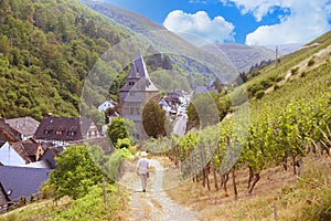 man walks along narrow road in gorge among old houses, watchtowers and vineyards in Middle Rhine valley above town of Bacharach in