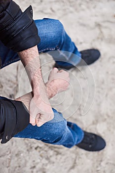 A man walks along the seashore, sits and thinks with his hands clasped. Closeup on a man hands and legs. Thinking about everything