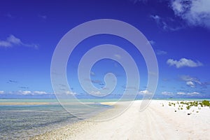 A man walks along a white sandy beach next to a turquoise lagoon on the island of Fakarava in the South Pacific