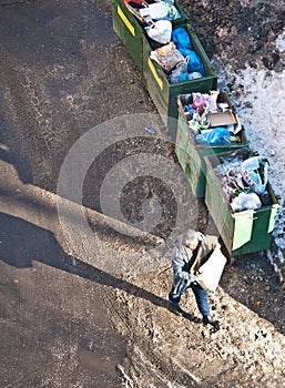 Man walks with a carton box along the overloaded dumpsters in winter street