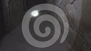 A man walks through a dark old abandoned basement and shines a flashlight