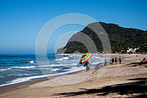 A man walks down the sandy beach holding a rainbow umbrella on the coast of the Pacific Coast