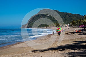 A man walks down the sandy beach holding a rainbow umbrella on the coast of the Pacific Coast