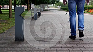 A man walks down the street and throws a plastic bottle by the garbage