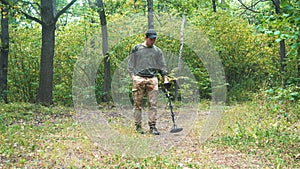 man walks with a metal detector through the forest