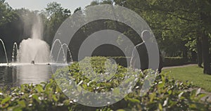 A man walks through a natural park past a fountain on a hot sunny summer day.