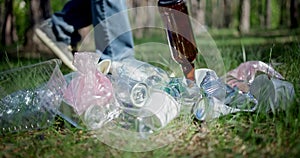 A man walks past a pile of garbage in the forest and throws a glass bottle at it