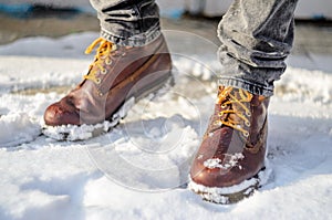 Man walks in the snow. Feet shod in brown winter boots.