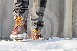 Man walks in the snow street. Feet shod in brown winter boots.