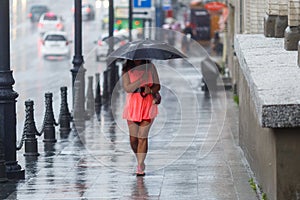A man walks under an umbrella during the rain, having his face off the camera